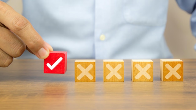 Hand choose check mark on cube wooden toy block with cross symbol