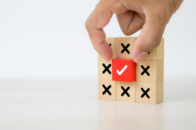 Hand choose check mark on wooden block stacked with cross symbol.