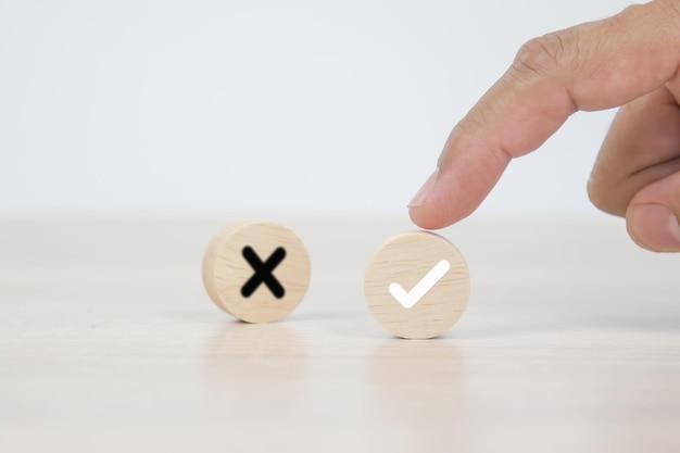 Hand choose check mark on wooden block stacked with cross symbol