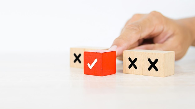 Hand choose check mark on wooden block stacked with cross symbol