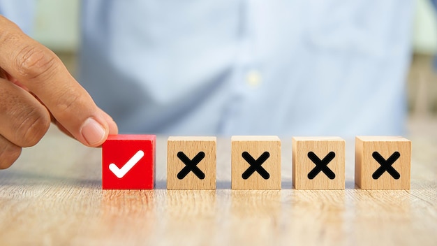 Hand chooses check mark on wooden toy with cross symbol