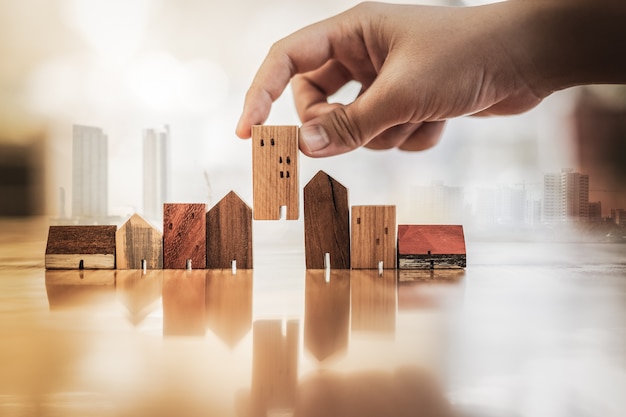 Hand choosing mini wood house model from model on wood table