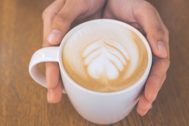 hand and cup of hot latte art coffee on wooden table