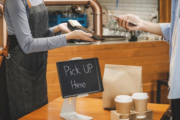 Hand customer using digital mobile phone scan QR code pay buying coffee with waitress staff in apron and hot black coffee cup and dessert paper bag on desk in cafe coffee shop cafe restaurant concept