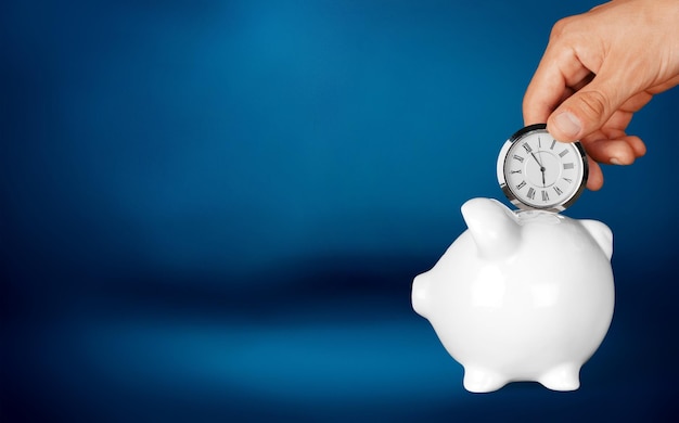 Hand depositing  clock  in piggy bank on background