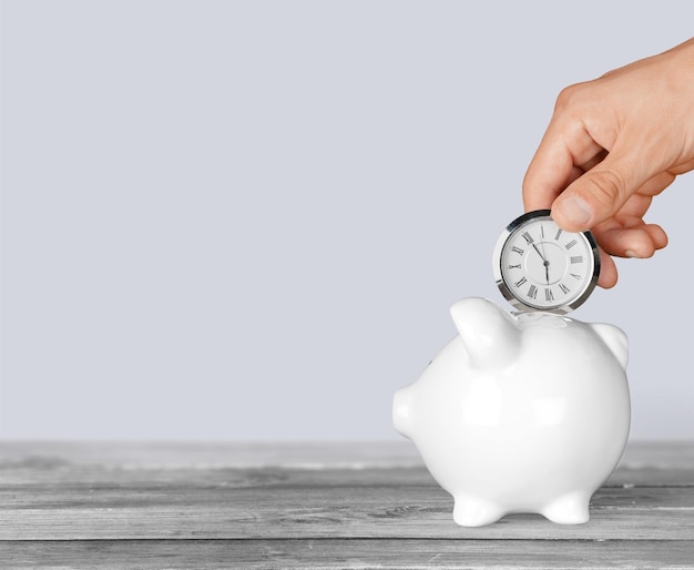 Hand depositing clock in piggy bank