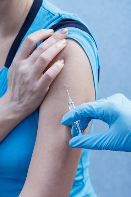 Hand of doctor in blue glove holding syringe for vaccination to upper arm of patient