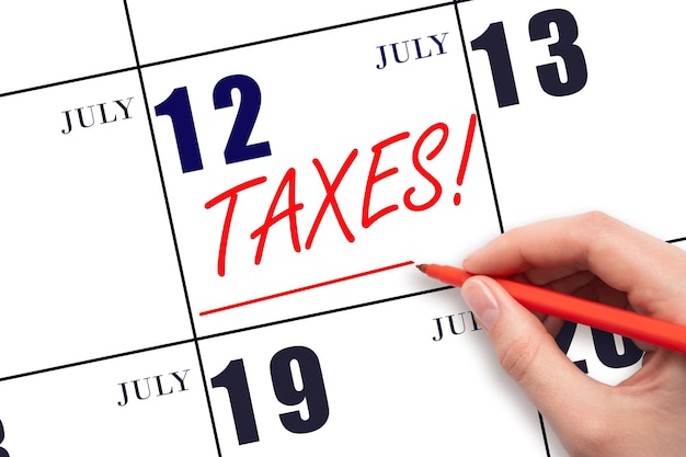 Hand drawing red line and writing the text Taxes on calendar date July 12 Remind date of tax payment