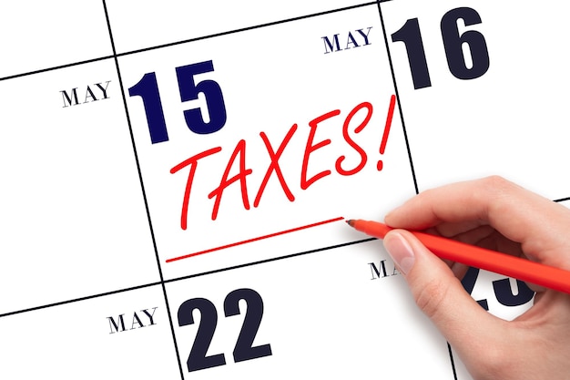 Hand drawing red line and writing the text Taxes on calendar date May 15 Remind date of tax payment