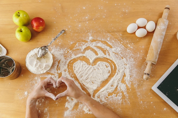 The hand drawn heart in flour on the kitchen table and other ingredients and tablet. Top view.