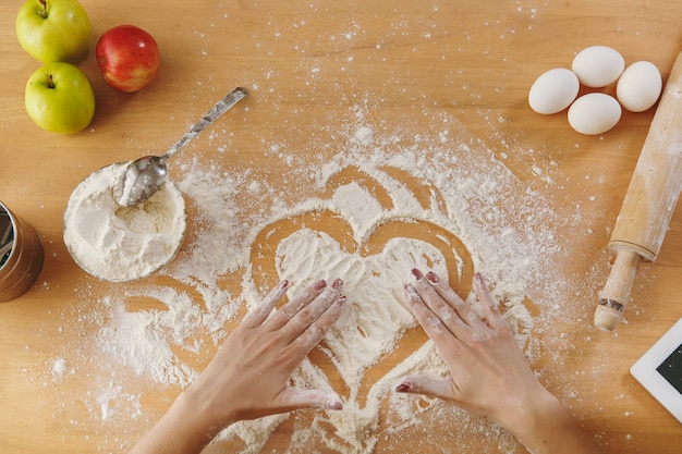 The hand drawn heart in flour on the kitchen table and other ingredients. Top view.