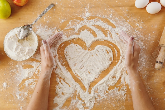 The hand drawn heart in flour on the kitchen table and other ingredients. Top view.