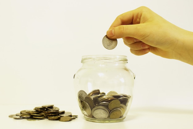 Hand drops money into a glass jar for a savings