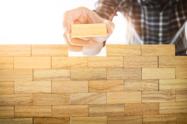 Hand of engineer playing a blocks wood tower game (jenga) on blueprint or architectural project concept.