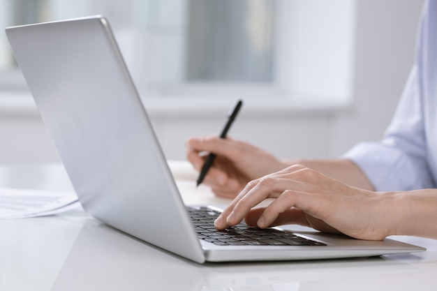 Hand of female employee pushing buttons of laptop keypad while sitting by desk and working over project