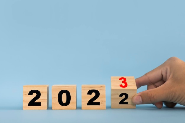 Hand flipping wooden blocks on blue background for change year 2022 to 2023 Setting goals for the upcoming new year