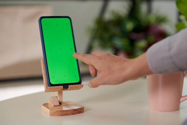 Hand and forefinger of young woman pointing at smartphone green screen