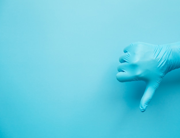 Hand gesture of doctor wearing blue gloves on blue background, sign for not good