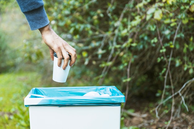 Hand getting rid of paper cup in rubbish