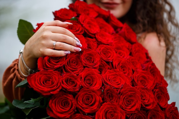 Hand of a girl with a wedding ring close-up on a bouquet of red roses