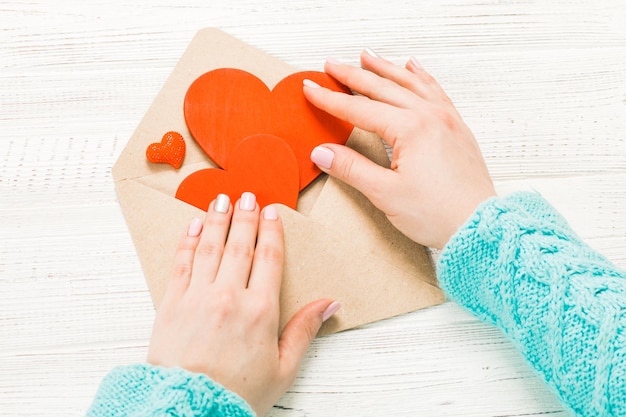 Hand of girl writing love letter on Saint Valentines Day Handmade postcard with red heart shaped figure 14 February holiday celebration Valentine day concept with copy space