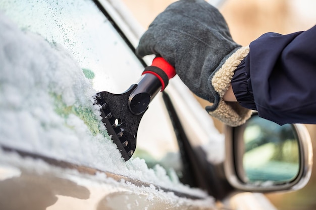 Hand in glove holding a snow scraper and removing ice from a car window