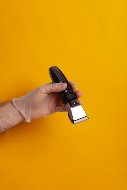 A hand in a glove holds a hair clipper