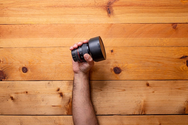 Hand grabbing camera lens on light wood background Labor Day