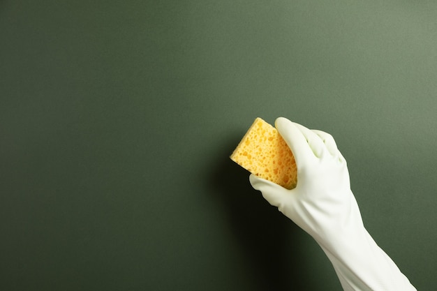 Hand in a green rubber glove holds a yellow   washing sponge over green background