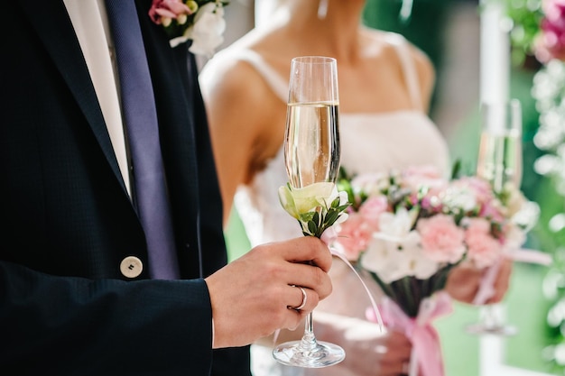 The hand groom's holds a glass of champagne on the background of the bride Wedding ceremony