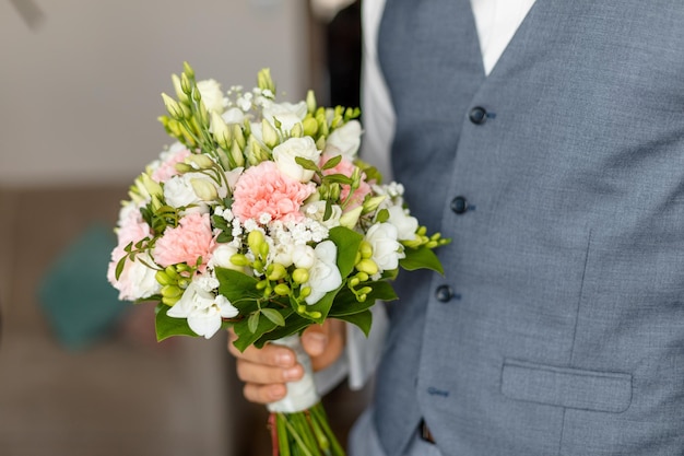 Hand of groom in wedding suit holding soft bridal bouquet of fresh flowers closeup elegant attribute