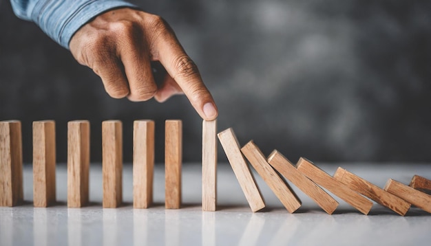 Hand halting wooden dominoes Symbolic of preventing business crises risk management and protectiv