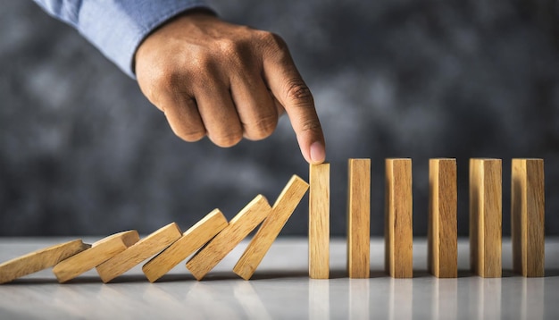 Hand halting wooden dominoes Symbolic of preventing business crises risk management and protectiv