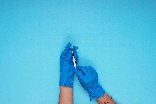 Hand held needle with blue glove on light blue background