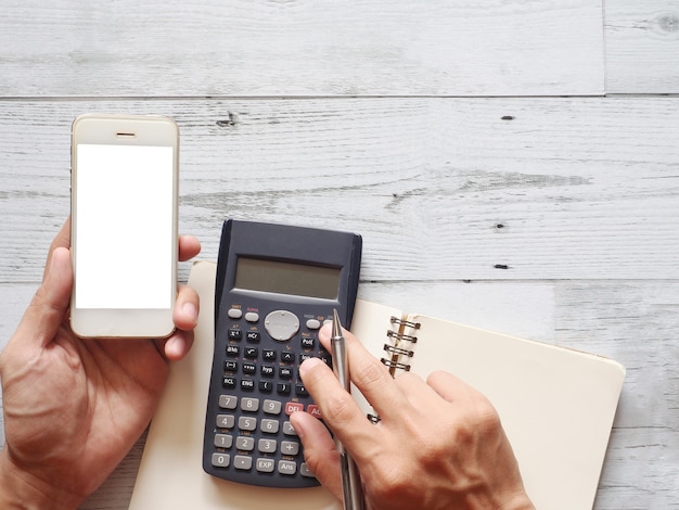 Photo hand hold cellphone white screen using calculator with cactus pen on table top view business concept