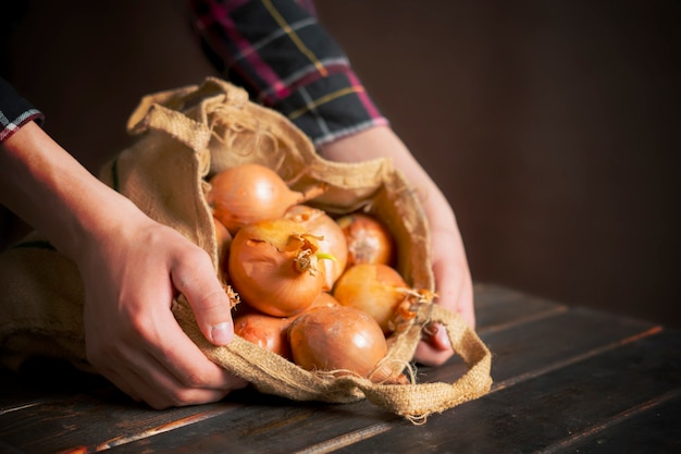 Hand hold fresh onion cloth bag isolated on wooden surface b