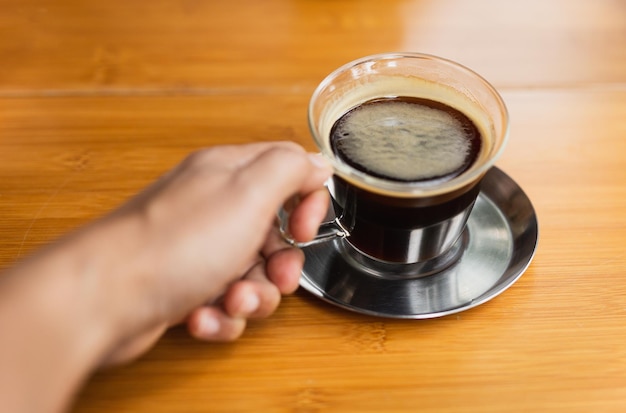 Hand holdign black coffee on wooden table