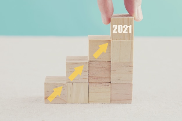 Hand holding 2021 and arrows ladder up on wooden blocks