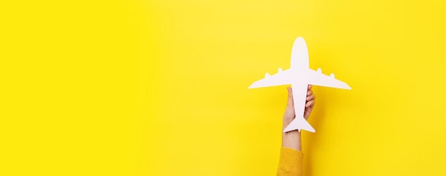 Hand holding airplane over yellow background, panoramic layout