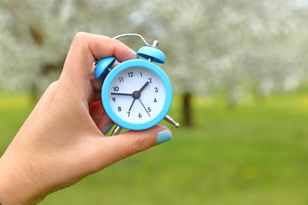 Hand holding an alarm clock with abstract nature background