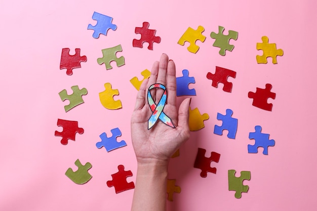 hand holding autism ribbon paper awareness surrounded by colorful pieces of puzzles