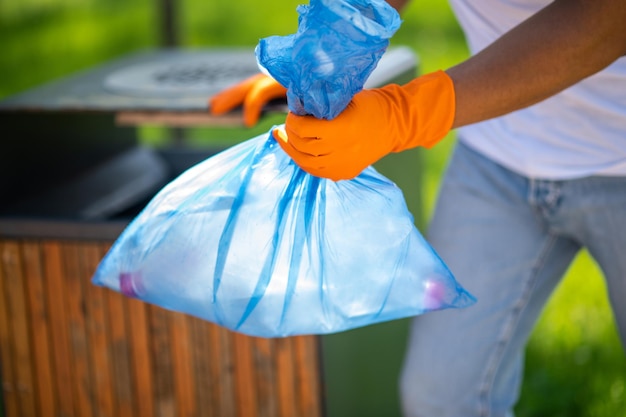 Hand holding bag with waste near trash can