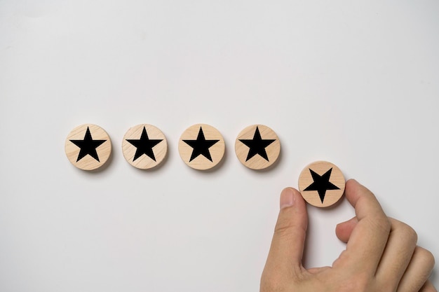 Hand holding black star which print screen on round wooden to give five stars for excellent evaluate after customer use product service ISO and quality standard certificate concept