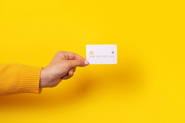 Hand holding blank white credit card mockup, card with electronic chip over yellow background