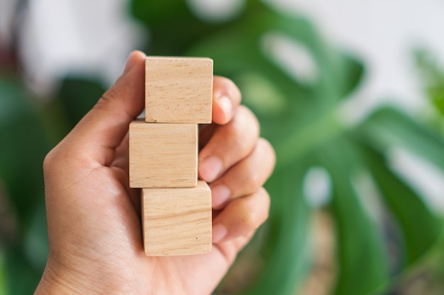 Hand holding blank wooden cubes with blurred plants background