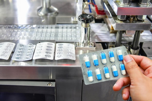 Hand holding blue capsule pack at medicine pill production line Industrial pharmaceutical concept