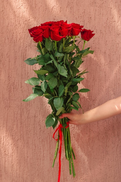  hand holding bouquet of red roses against rough wall