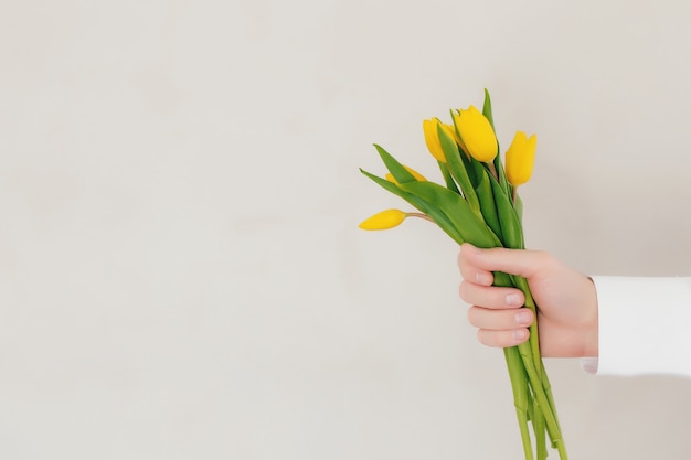 Hand holding bouquet with yellow tulip flowers on gray concrete background