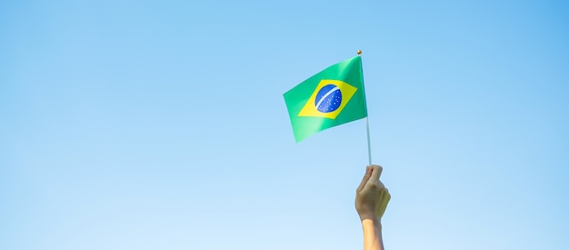 Hand holding Brazil flag on blue sky background. September Independence day and Happy celebration concepts