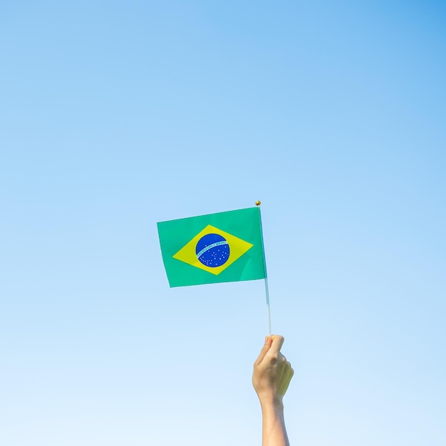 Hand holding Brazil flag on blue sky background September Independence day and Happy celebration concepts